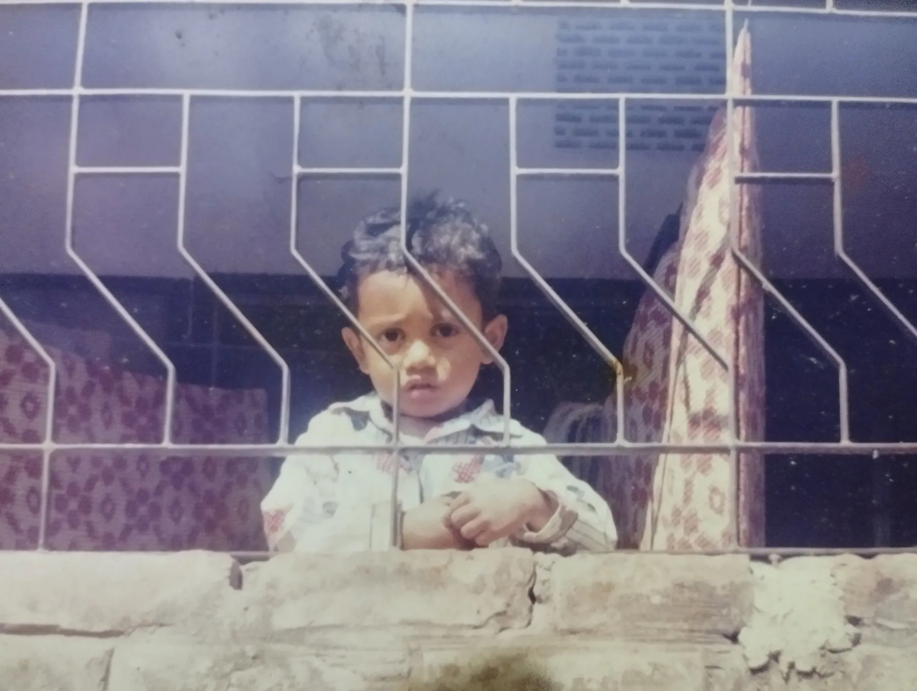 Maruf as a small child, looking out through a patterned window grill