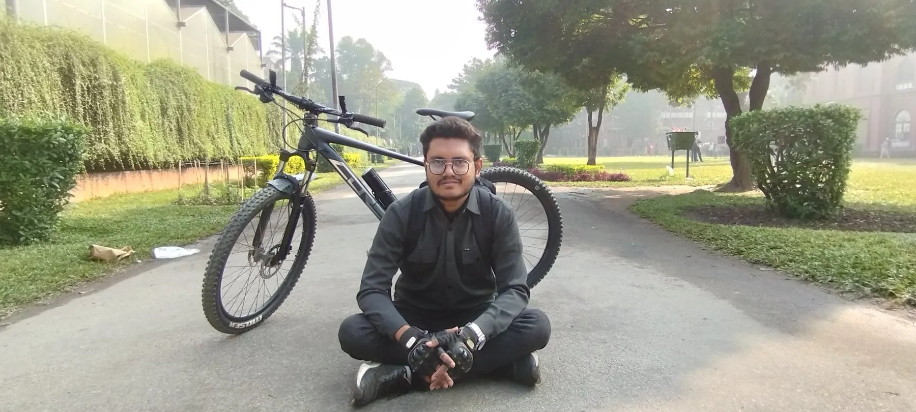 Maruf sitting cross-legged on a park path in front of his mountain bike