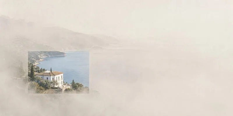 Thick fog over a coastline, with only one small clear patch showing a white villa above the sea.