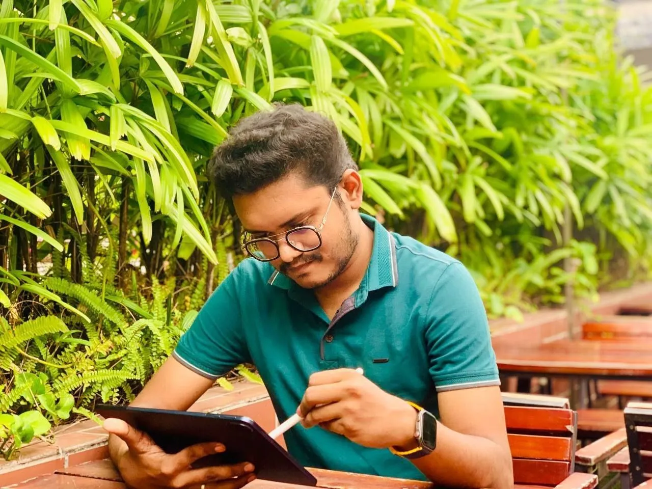 Maruf sketching on a tablet with a stylus, surrounded by green plants