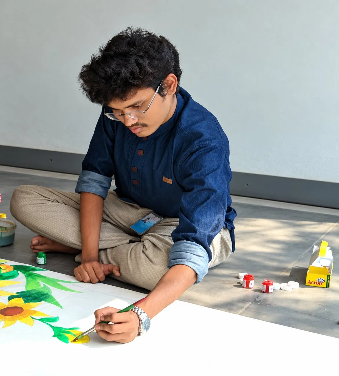 Maruf sitting on the floor painting yellow sunflowers on a large white board